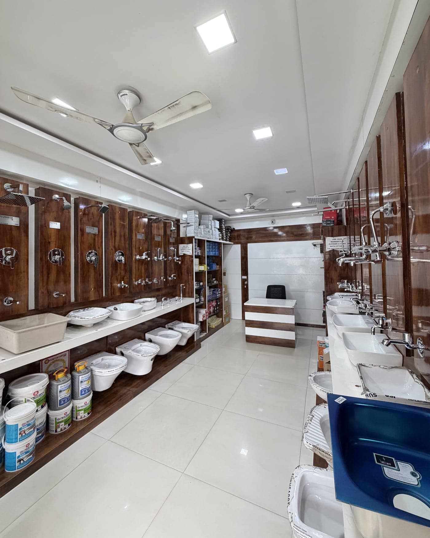 The showroom at Ghatlodia: taps and shower mixers on teak panels down one wall, basins and sanitaryware on the other, with the billing counter at the far end.