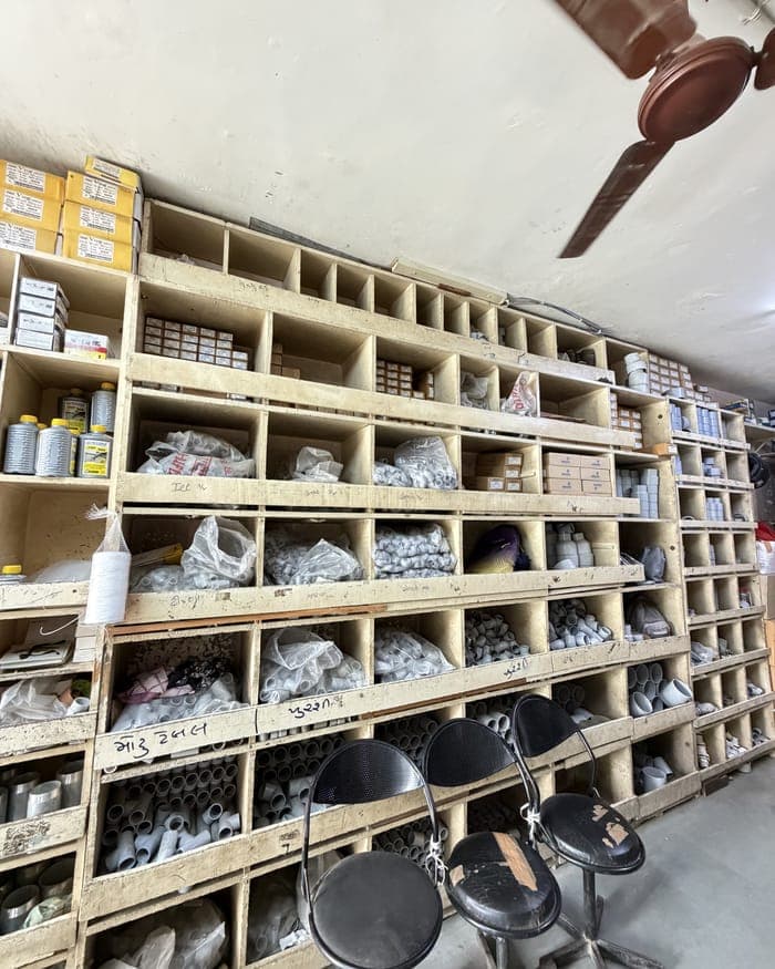 Wooden pigeonhole racks running the length of a room, every hole filled with plumbing fittings and labelled by hand in Gujarati.